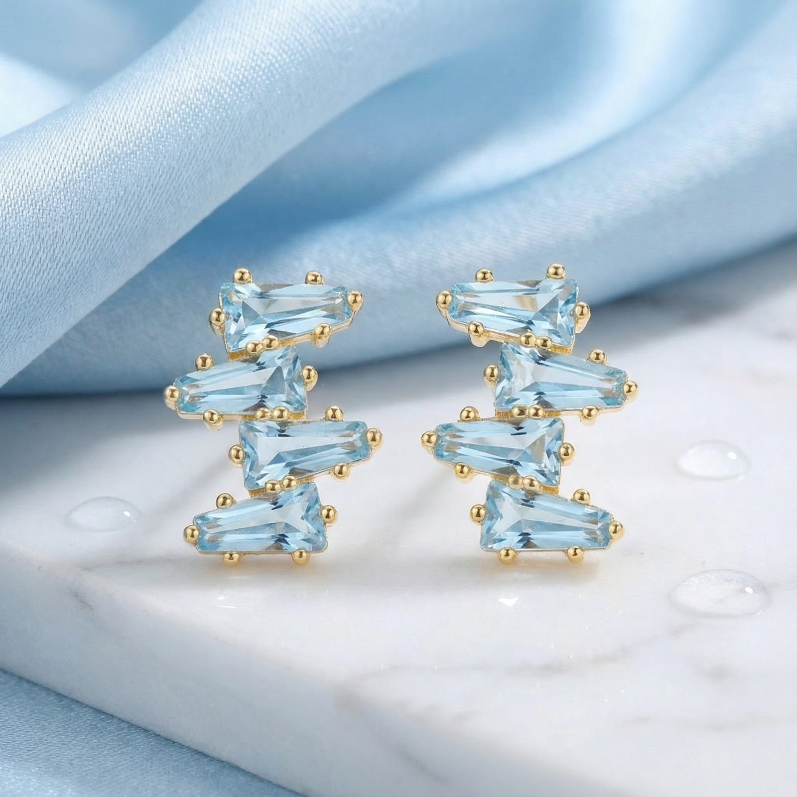 Front view of 18K gold vermeil cluster earrings with tapered baguette simulated aquamarine on a marble surface.
