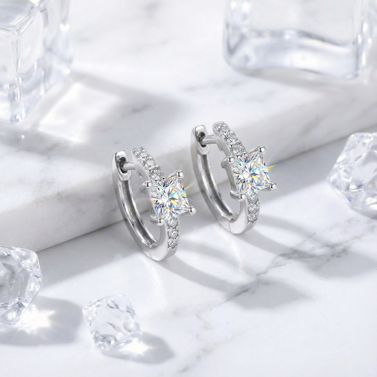 Princess-cut simulated diamond huggie earrings in S925 sterling silver on a marble surface with ice cubes.