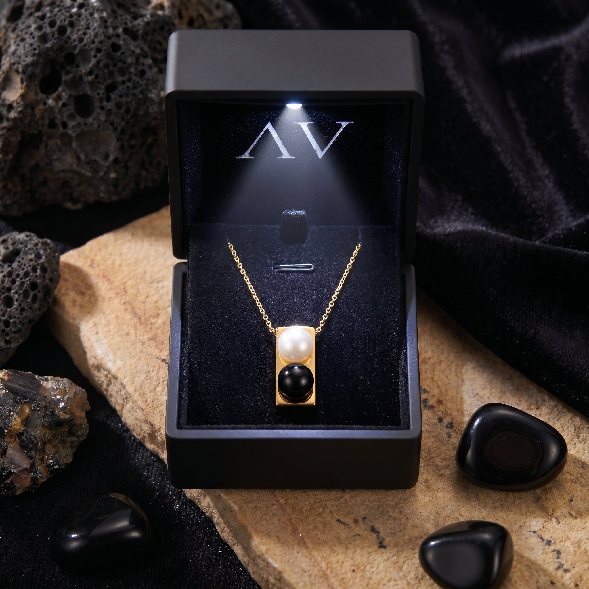 Gold Equilibrium Onyx Necklace presented in a black LED-lighted gift box on a styled stone surface.