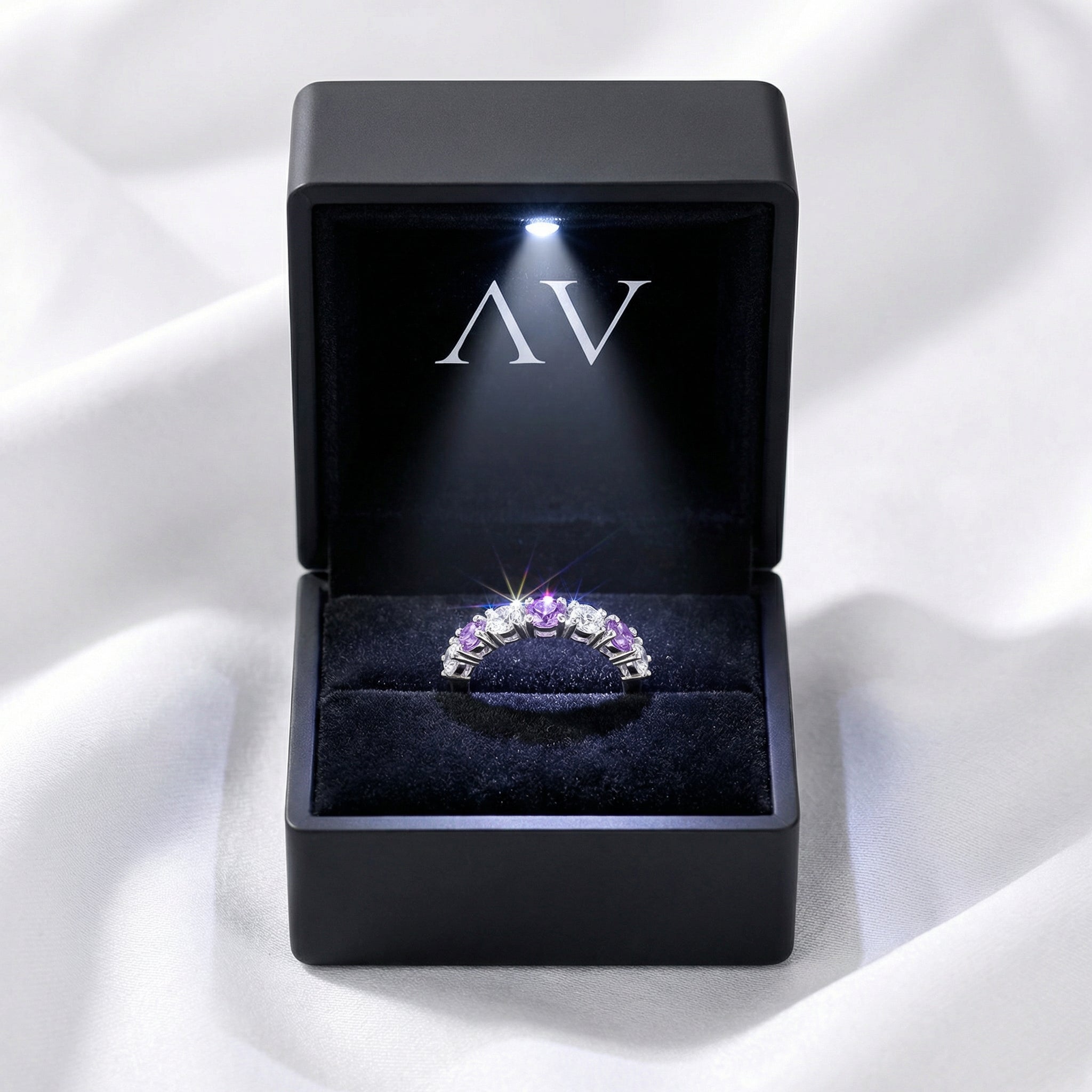 Amethyst eternity ring presented in a black LED-lit jewelry box with AV branding on white fabric.
