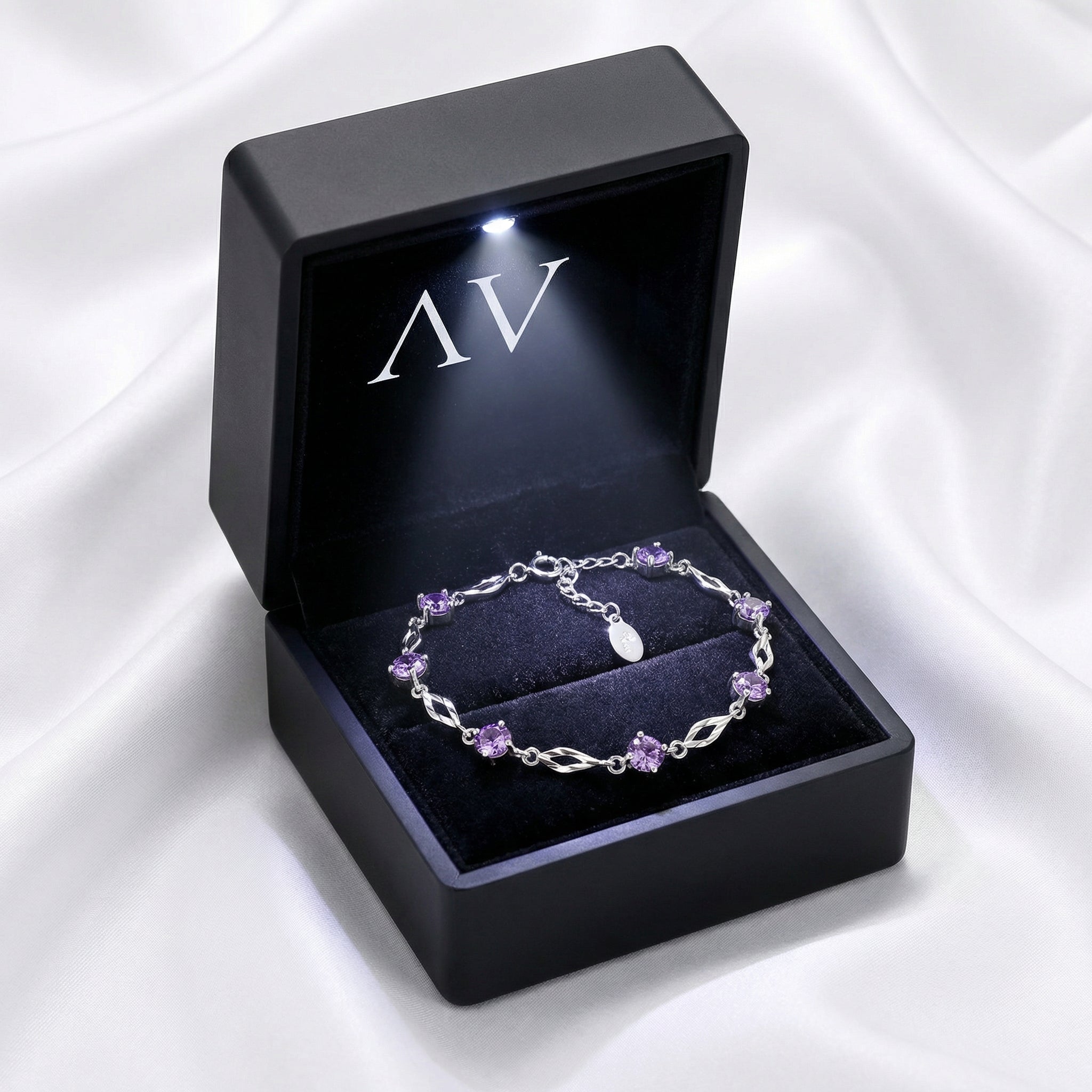 Sterling silver amethyst station bracelet inside a black LED-lit gift box on a white silk background.