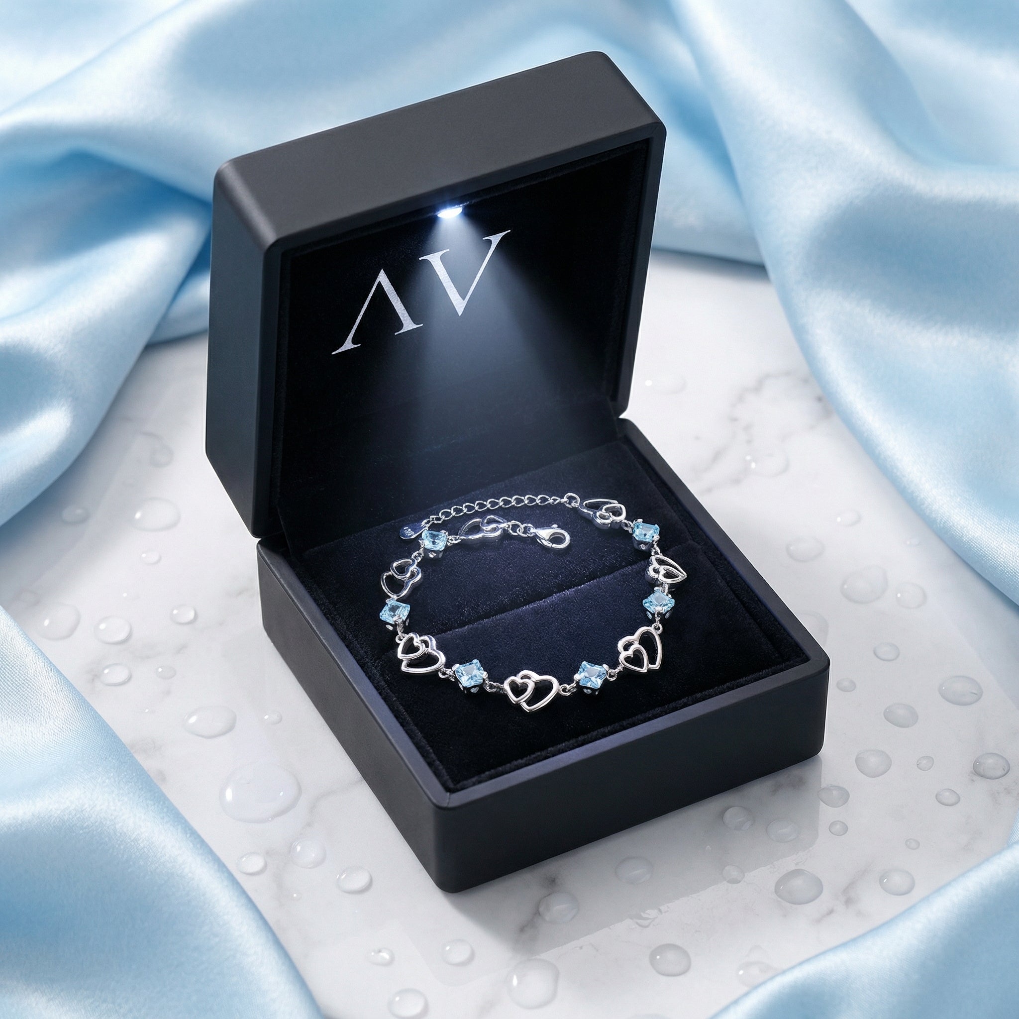 Sterling silver heart bracelet with blue stones in a premium black LED-lit gift box on blue silk.