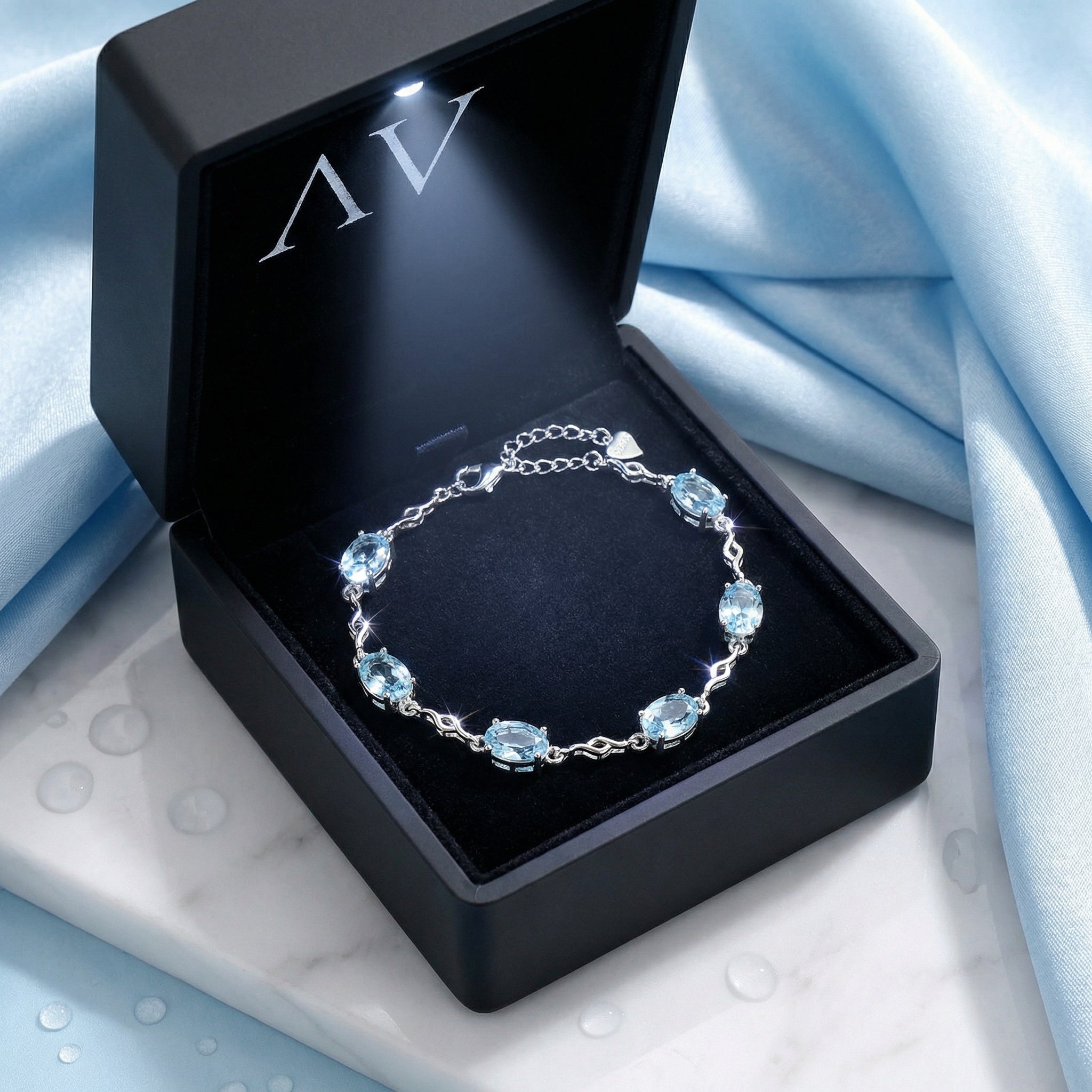 Sterling silver simulated aquamarine station bracelet presented in a black LED-lit jewelry gift box.