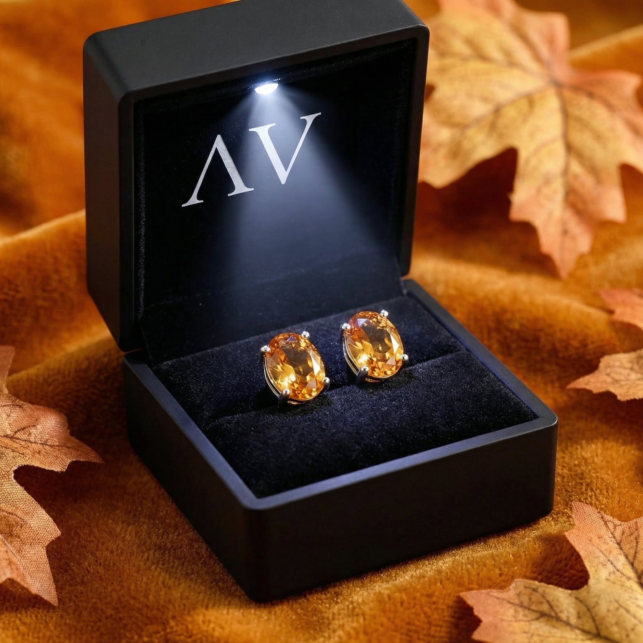 Oval simulated topaz stud earrings presented in a lighted black jewelry gift box on velvet.