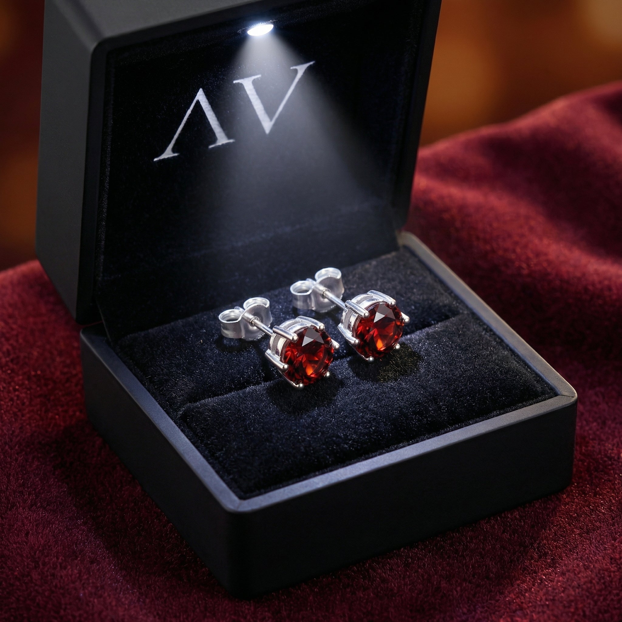 Red garnet stud earrings in sterling silver presented in a black LED-lit jewelry gift box.