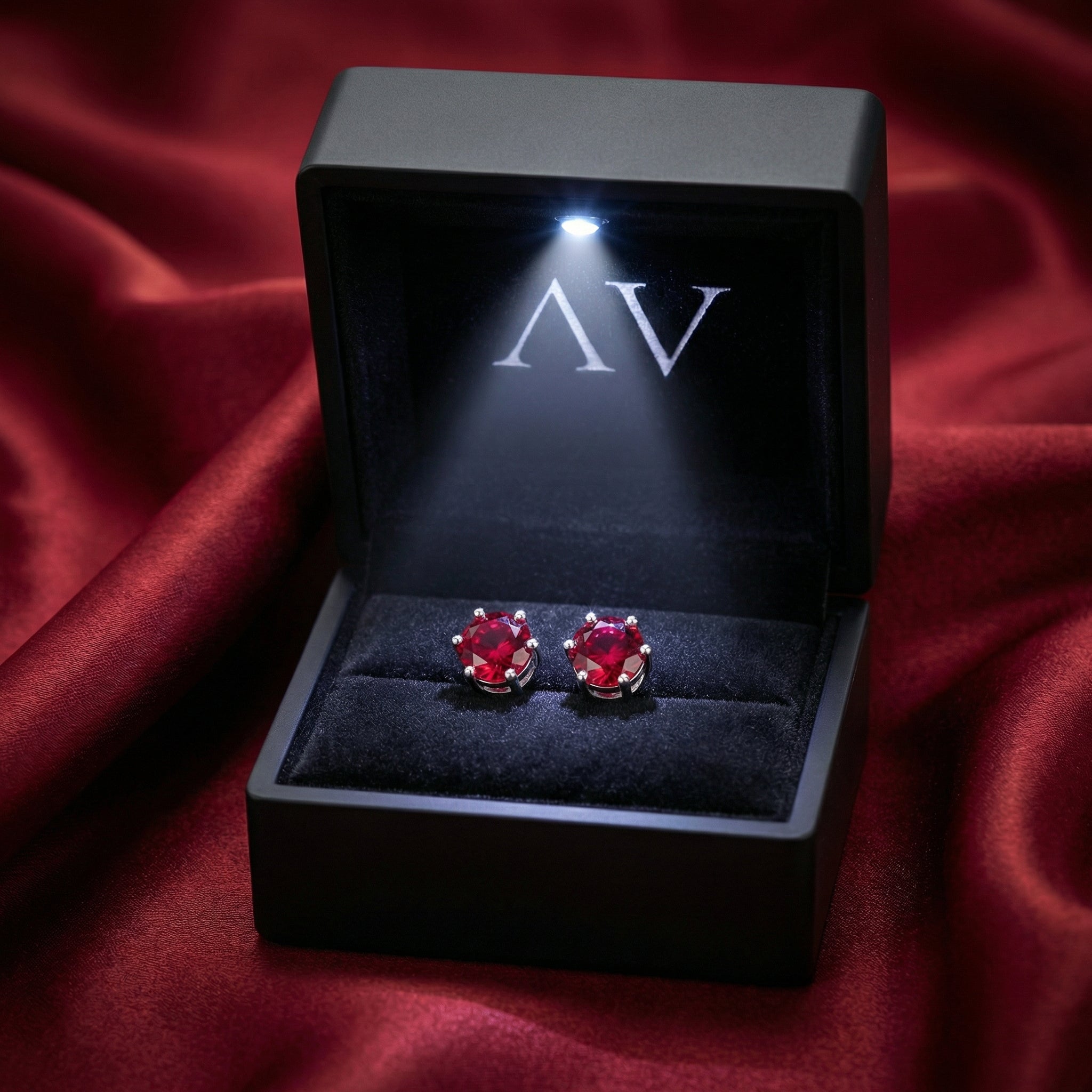Round cut simulated ruby silver stud earrings presented in a black LED-lit jewelry box.