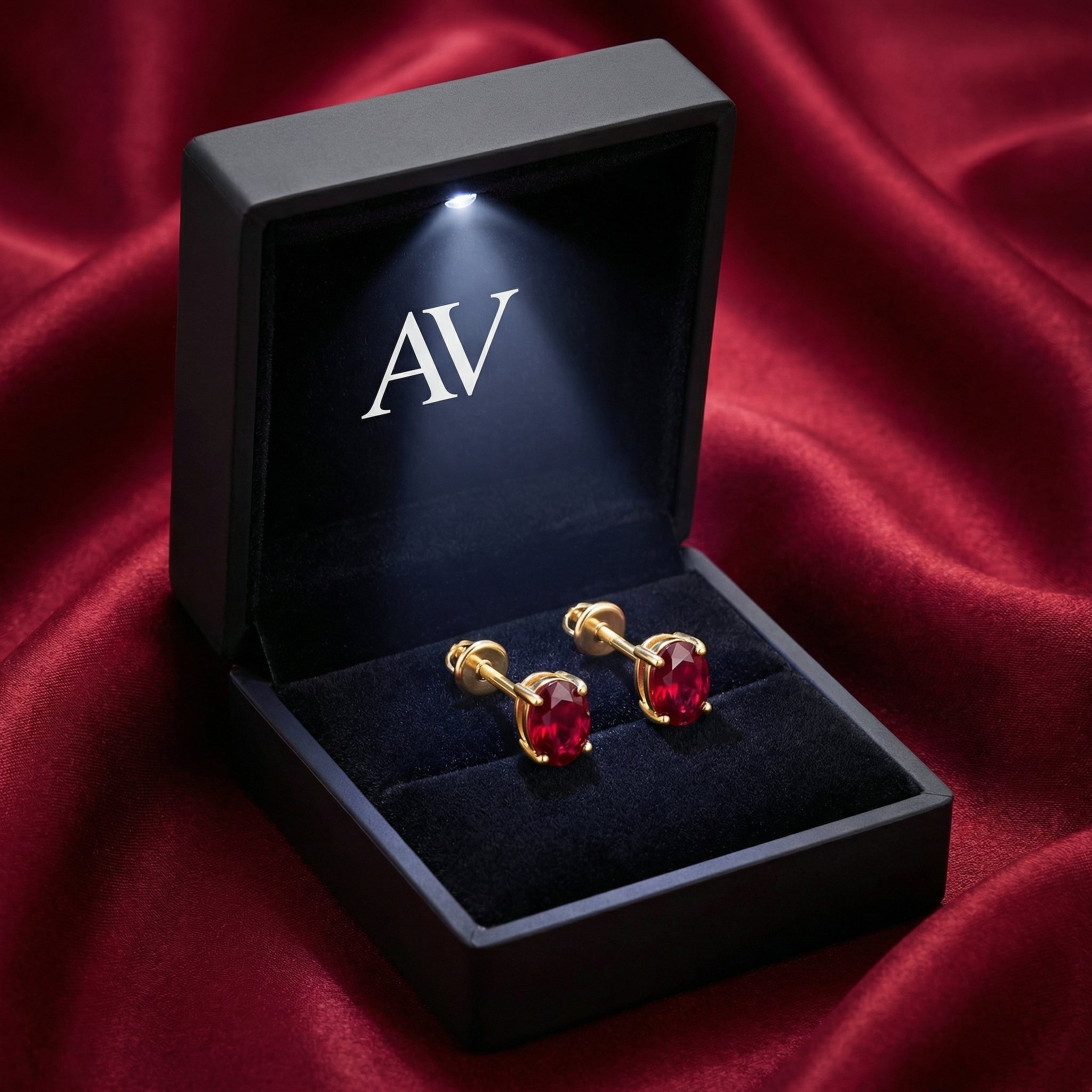Angled view of 18K gold vermeil oval ruby stud earrings inside a lighted black presentation box.