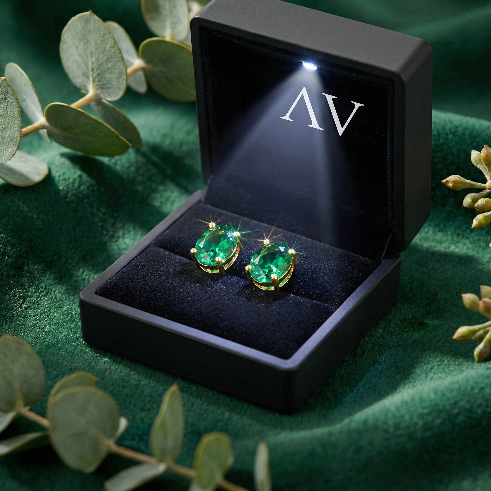 Oval simulated emerald stud earrings in 18K gold vermeil inside a black lighted jewelry presentation box.