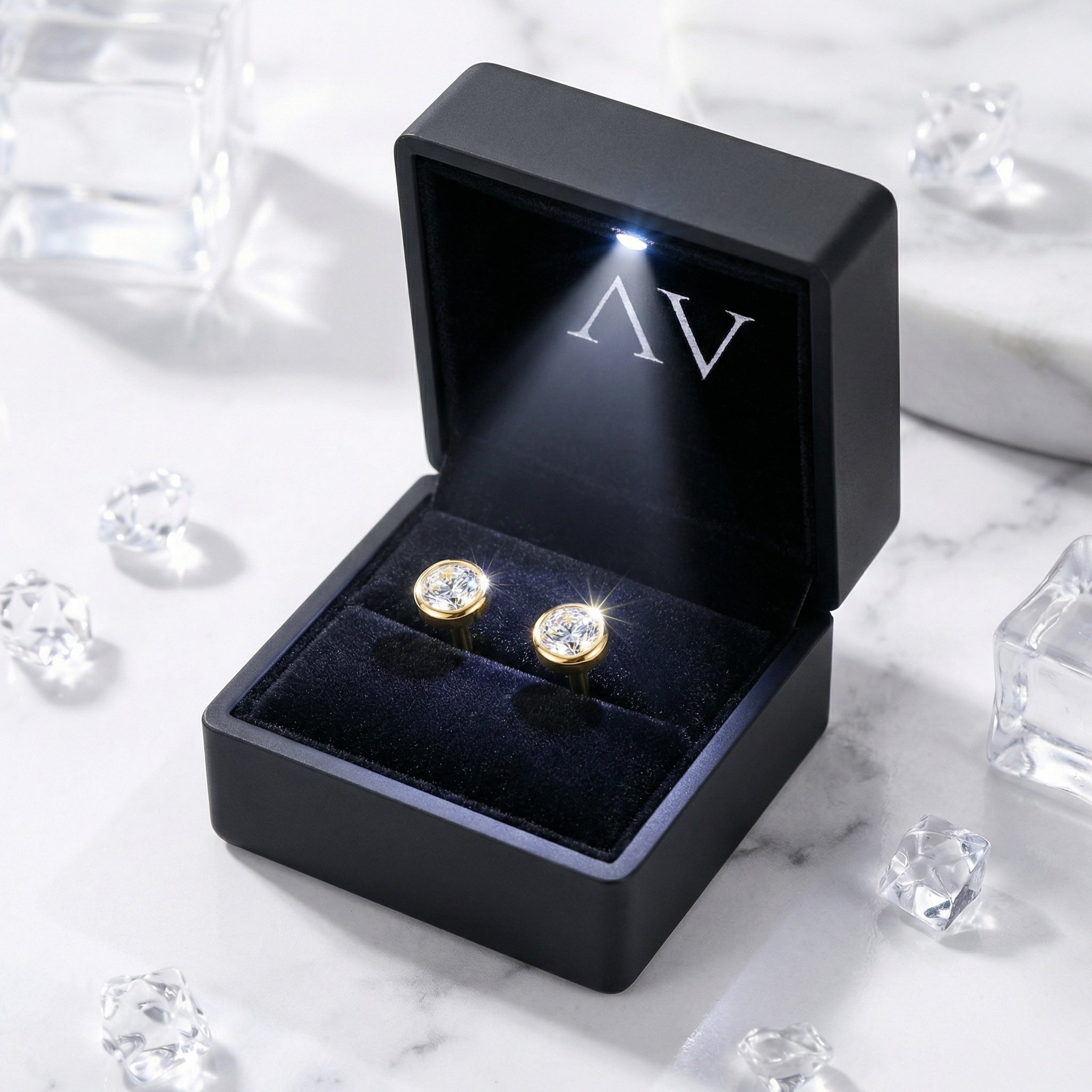 Gold vermeil bezel stud earrings inside a black LED-lit jewelry gift box on a marble background.