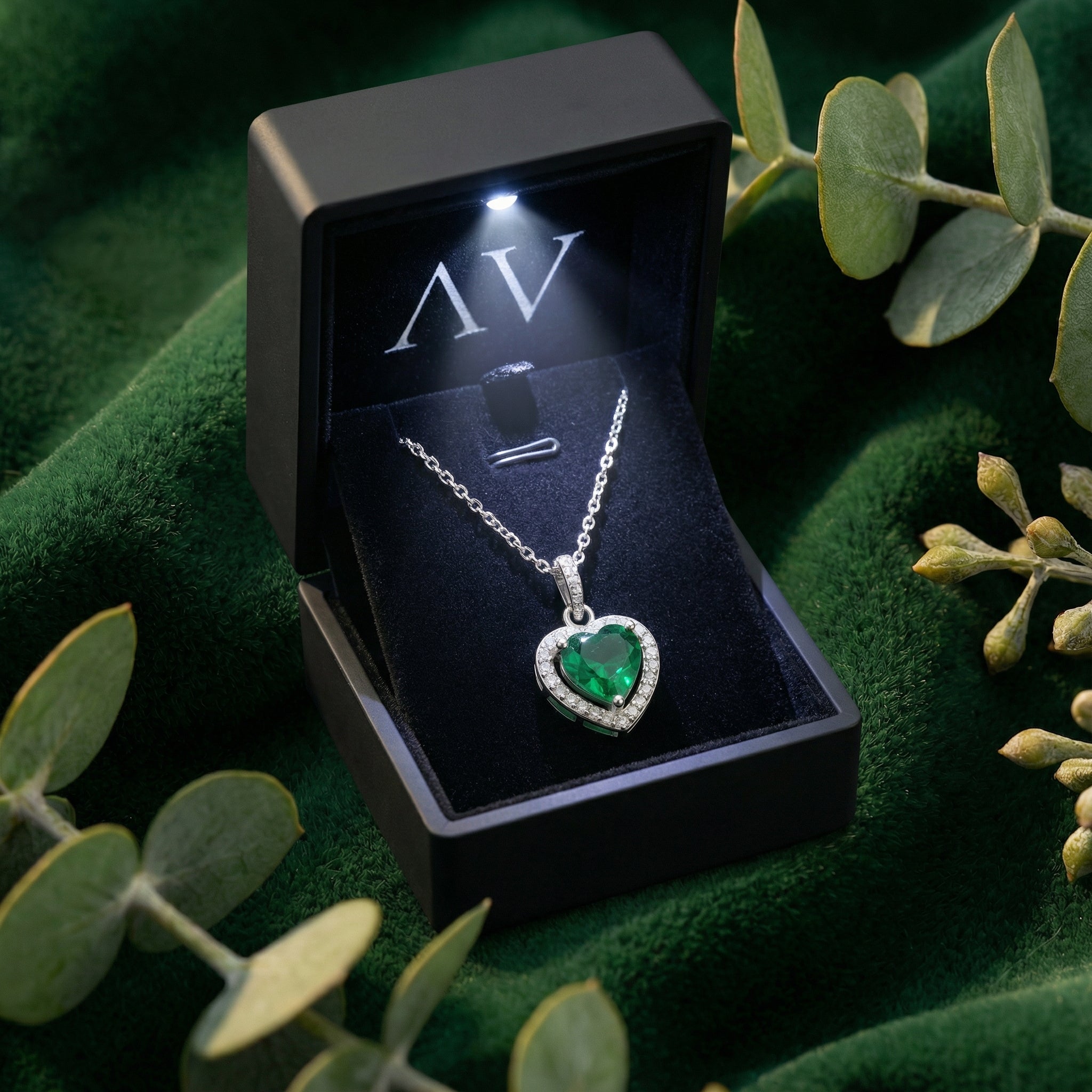 Heart-cut simulated emerald necklace in a lighted black gift box on a green velvet background.