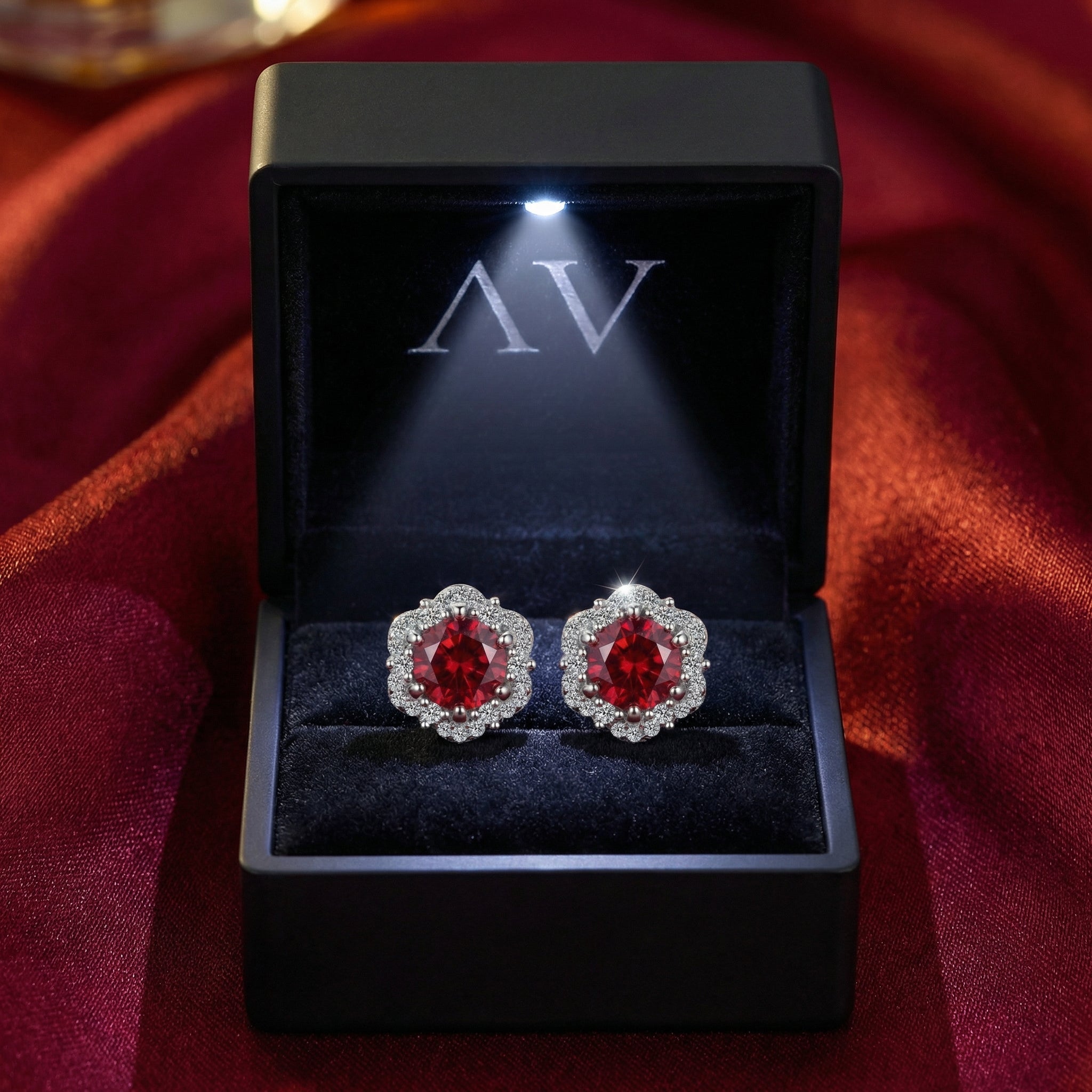 Simulated ruby halo stud earrings in a black LED-lit jewelry gift box on red silk.
