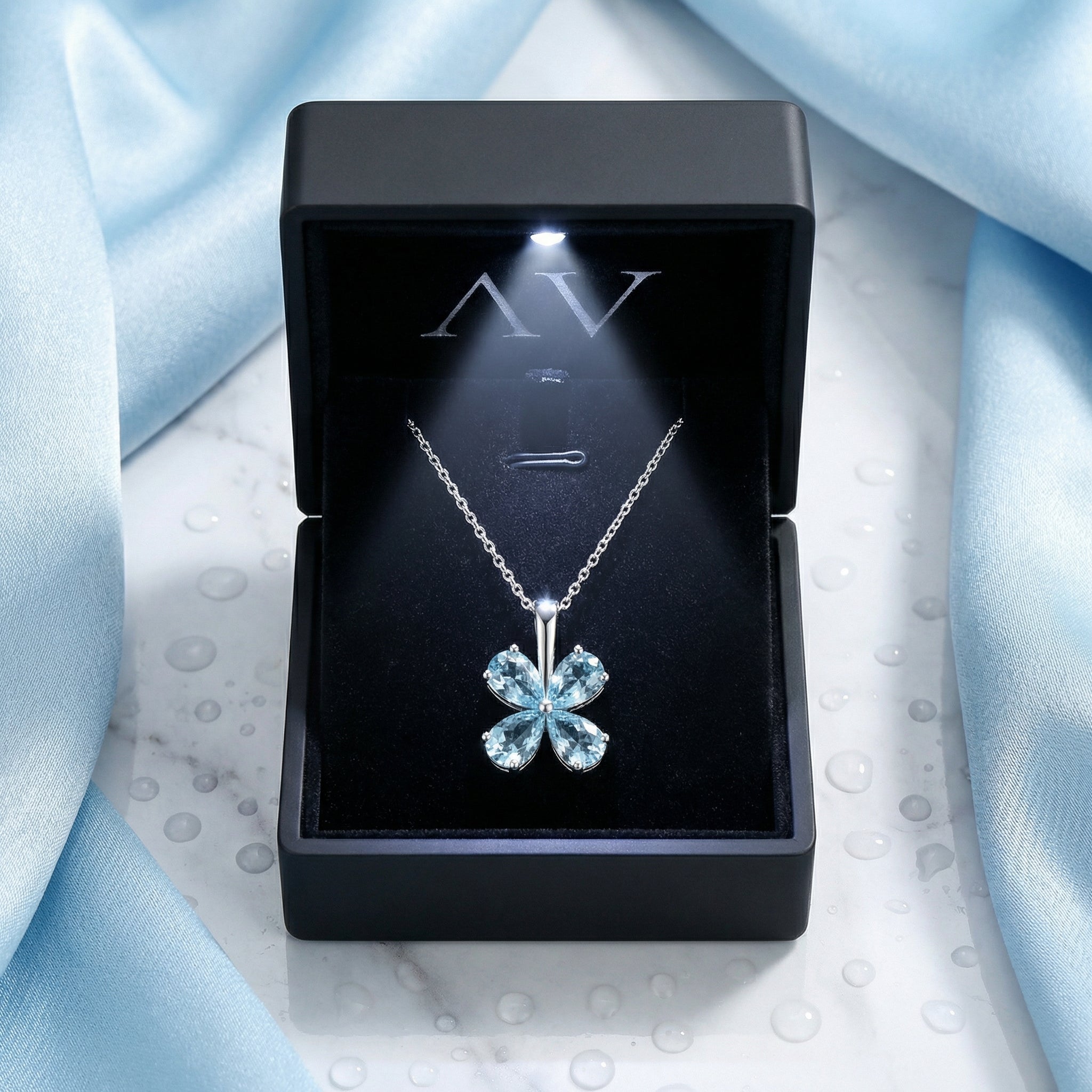 Solara clover necklace with pear-cut simulated aquamarines presented in an open black light-up jewelry box on marble.