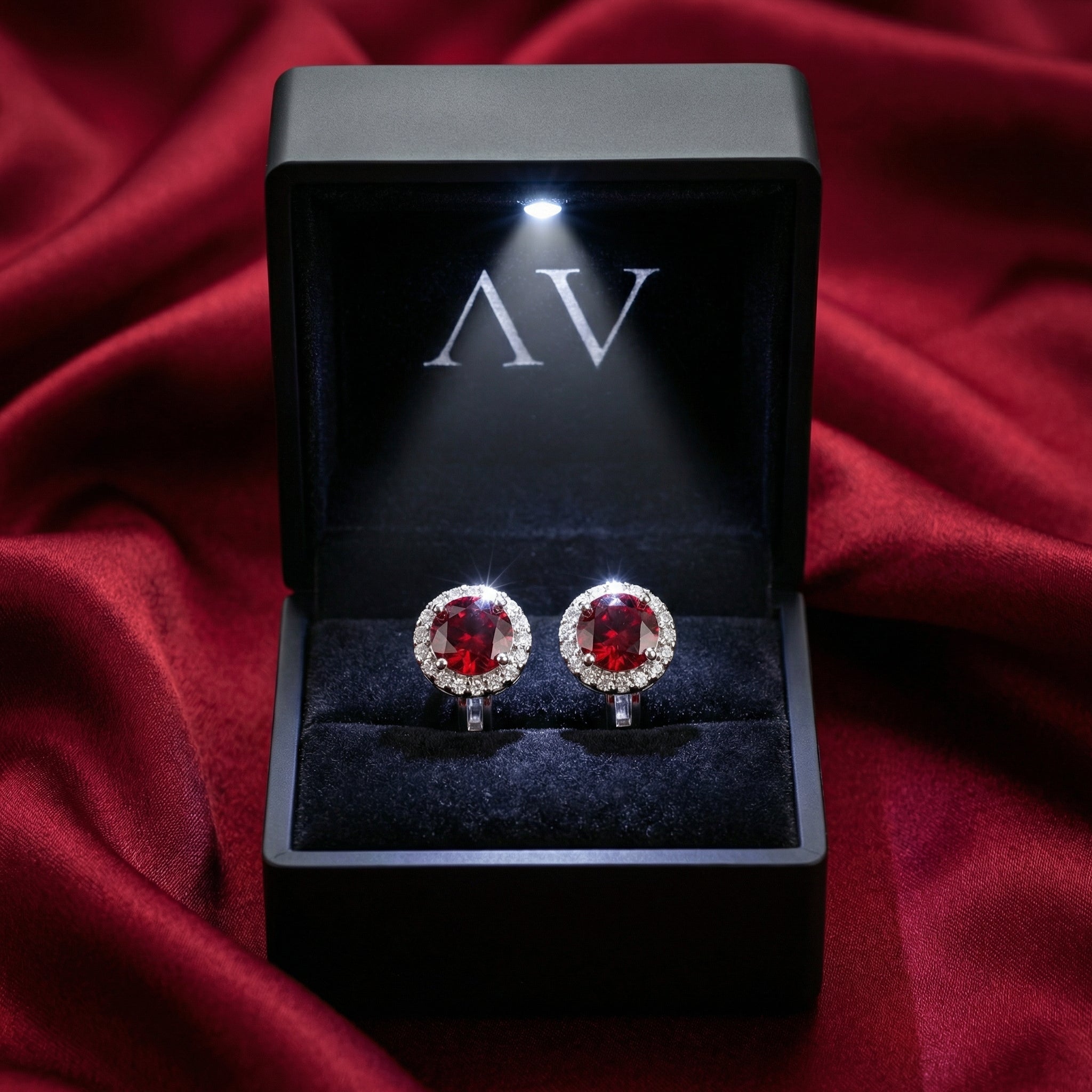Frontal view of silver and red ruby halo earrings inside an illuminated black jewelry box.