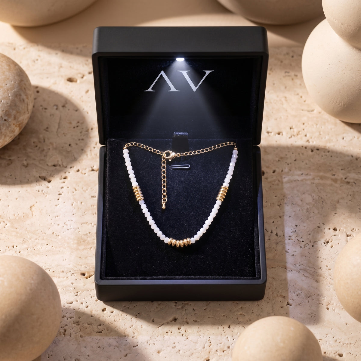 White quartz beaded necklace with gold accents inside a lighted black jewelry gift box.