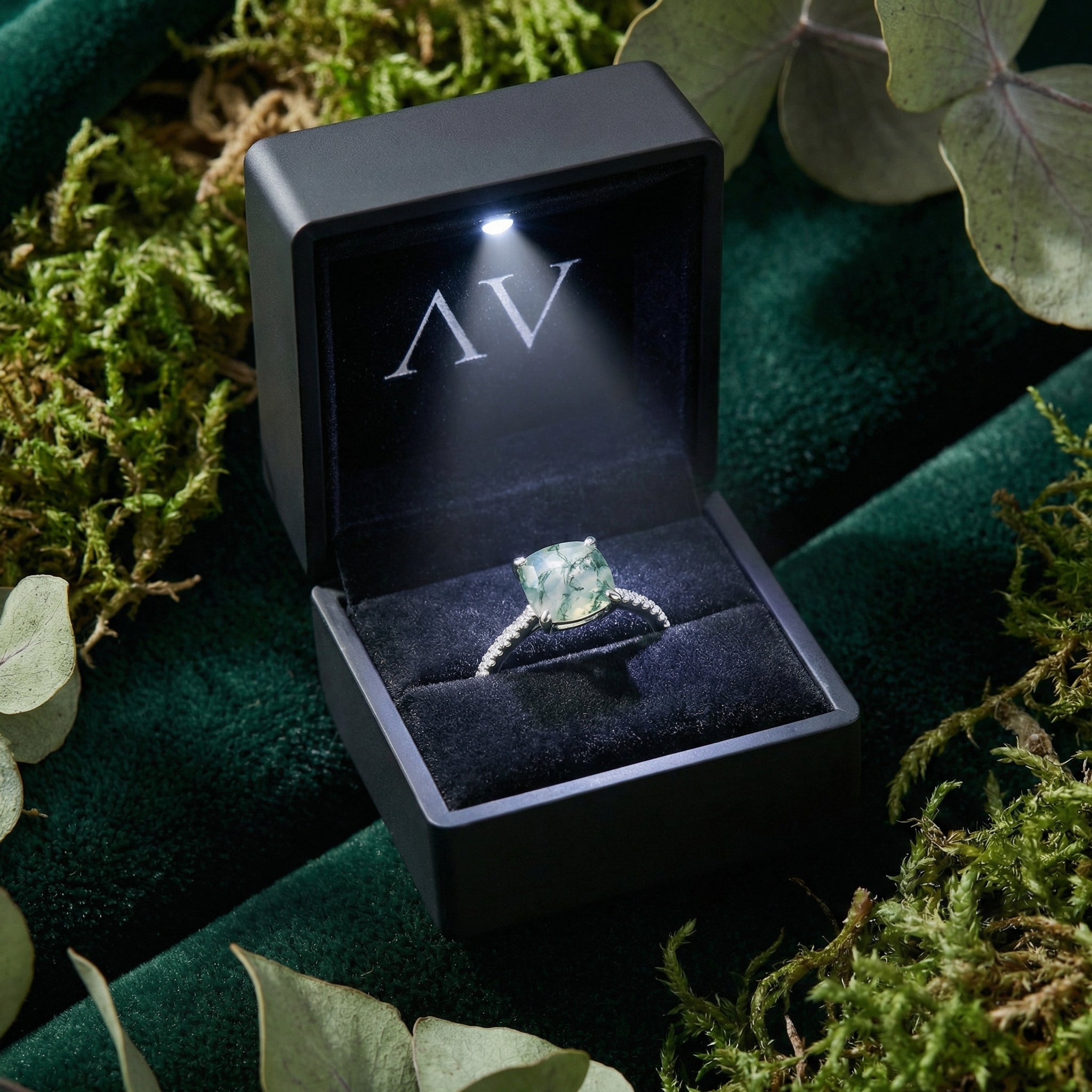 Cushion cut moss agate S925 sterling silver ring inside a black LED-lit gift box on green moss.