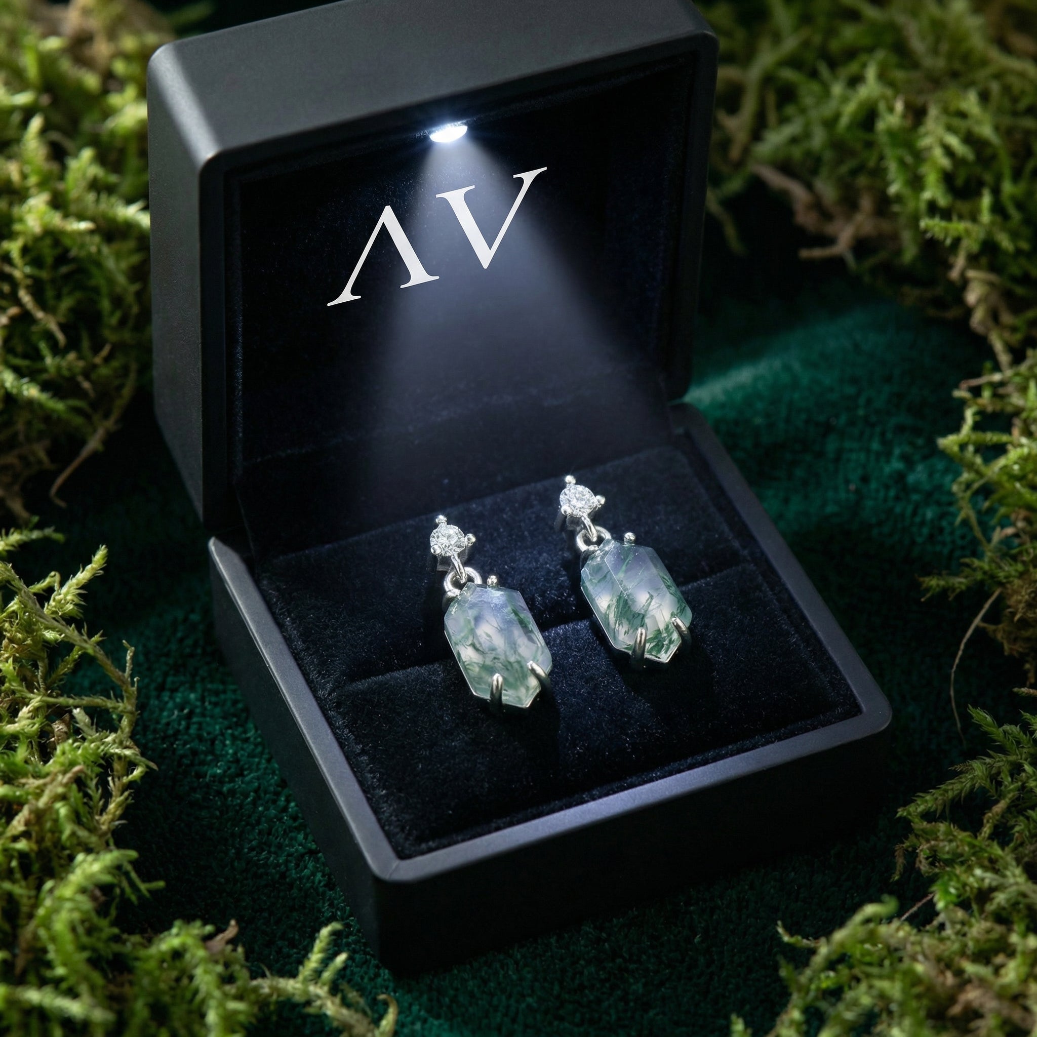 Barrel cut moss agate earrings in S925 sterling silver presented in a black lighted gift box on moss.