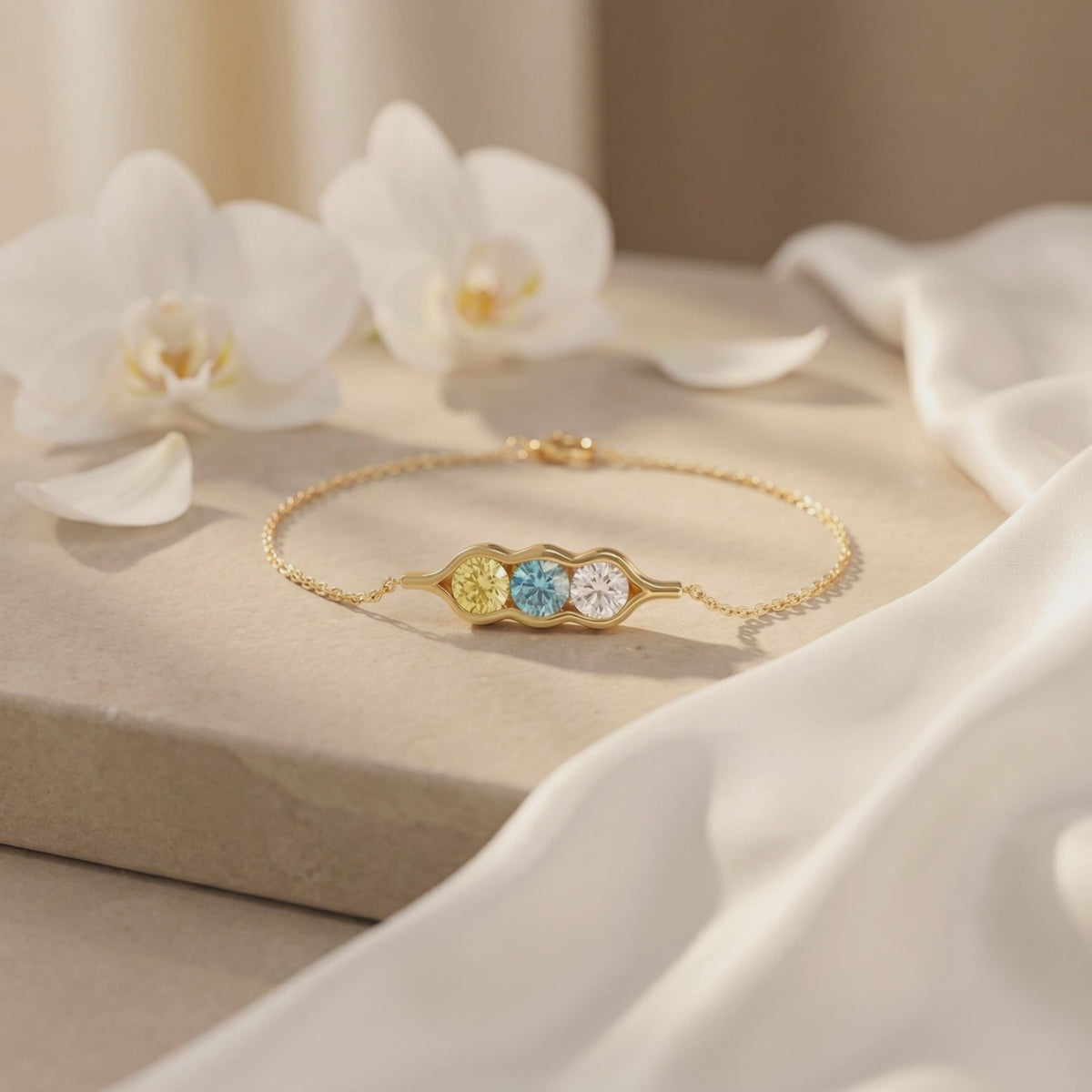 Gold-tone pea pod bracelet with yellow, blue, and clear gems laid flat on a stone surface near orchids.
