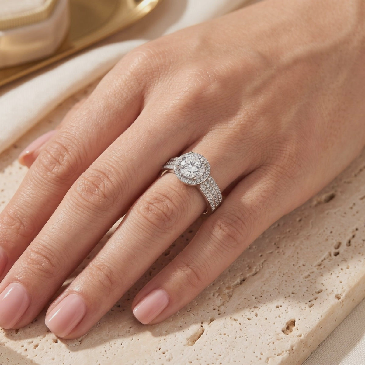 Silver halo ring with a round clear center stone worn on a hand over a textured stone surface.