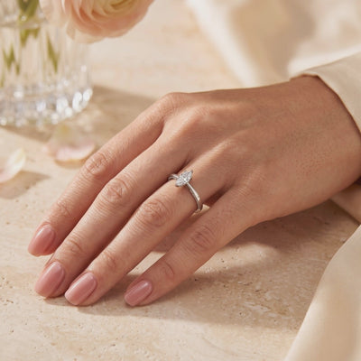 A hand wearing a silver ring with a marquise-cut clear stone and pavé accents along the shoulders.