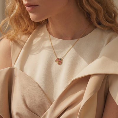 Model wearing the gold ladybug pendant necklace with red and blue enamel detailing.