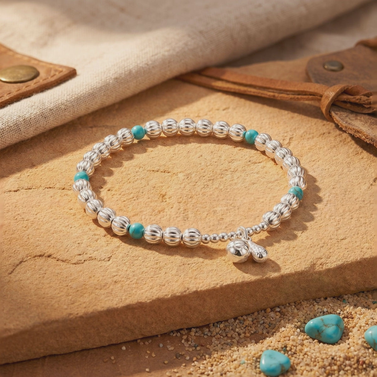 Silver bead bracelet with turquoise beads and a dangling silver charm arranged in a loop on a stone block