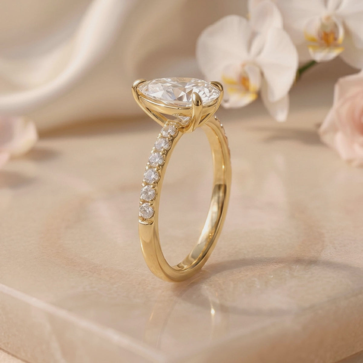 Side profile of a yellow-toned solitaire ring with a raised pear-cut stone and pavé band.