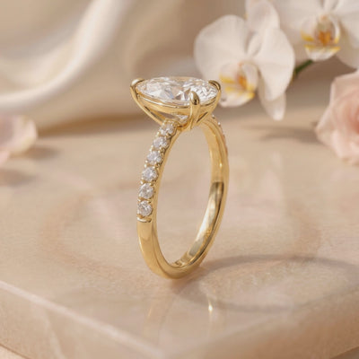 Side profile of a yellow-toned solitaire ring with a raised pear-cut stone and pavé band.