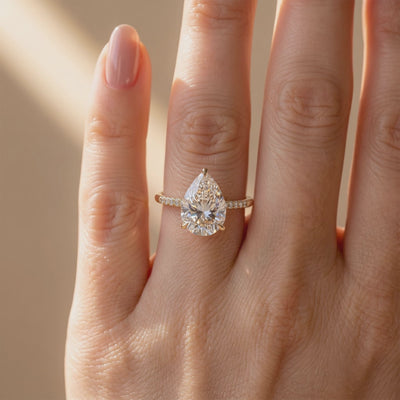 The Opaline pear-cut ring worn on a finger, shown from the front with a clear center stone and pavé band.