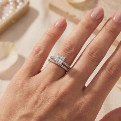 Silver ring set worn on a hand, featuring a princess-cut center stone and matching pavé band.