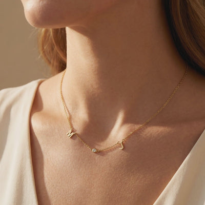Gold-tone necklace with M and J initials and a bezel-set round accent, shown worn on a model's neck.