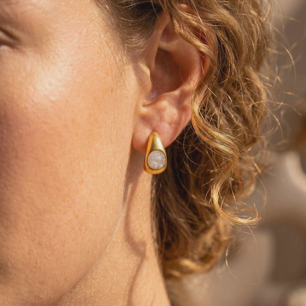 Close-up of a woman wearing a gold teardrop earring with a white textured inset.