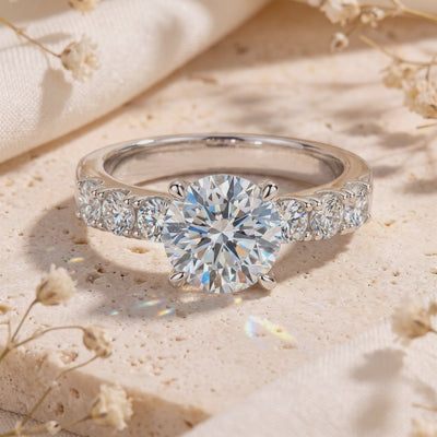 Close-up of a silver ring featuring a round clear center stone and side gems, resting on a textured stone surface.