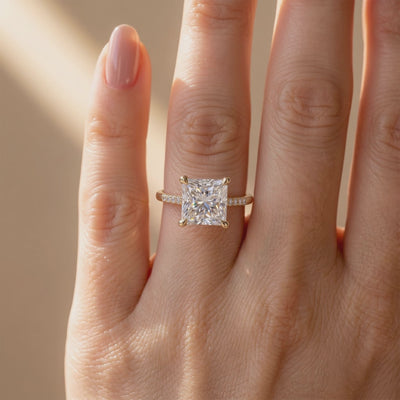 Princess-cut solitaire ring with a pavé band worn on a hand.
