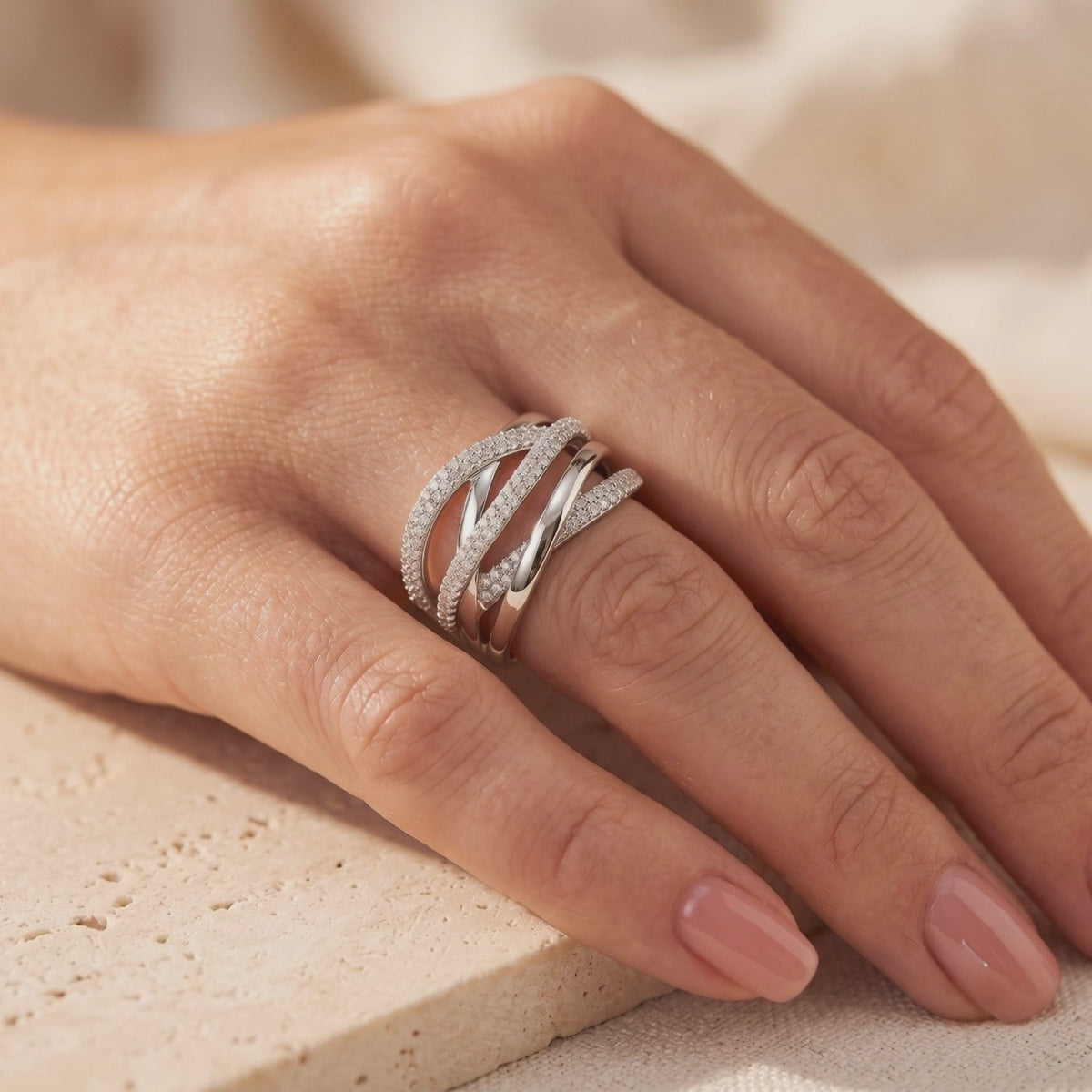 Wide silver crossover ring with multi-row pavé stones worn on a hand resting on a stone surface