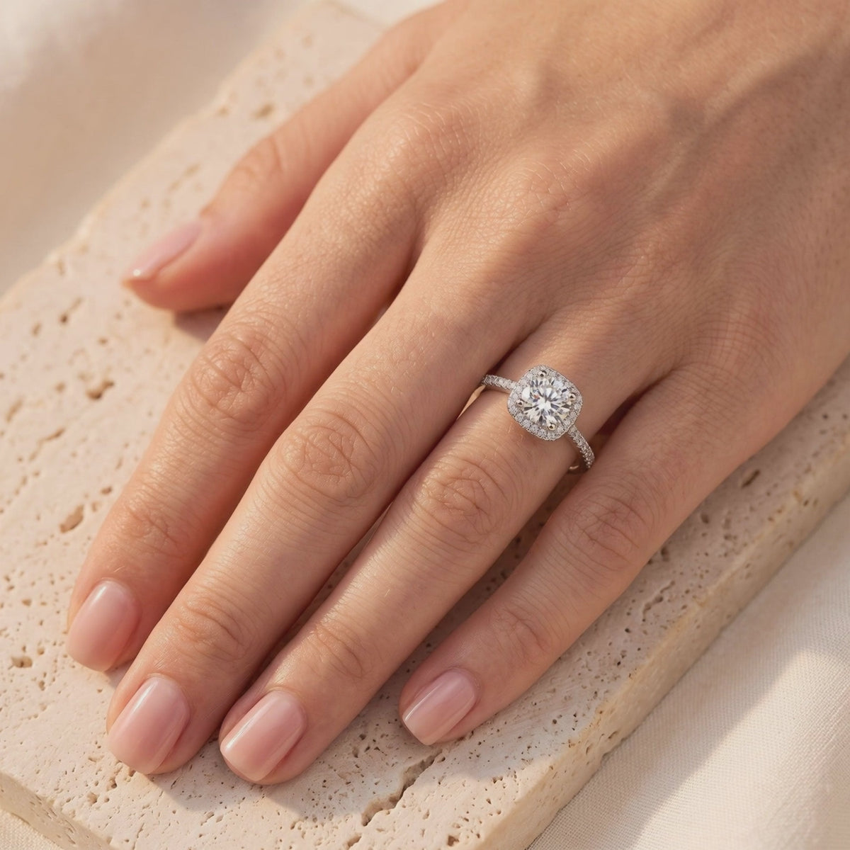 Silver halo ring with a round clear center stone, worn on a hand over a textured stone surface.
