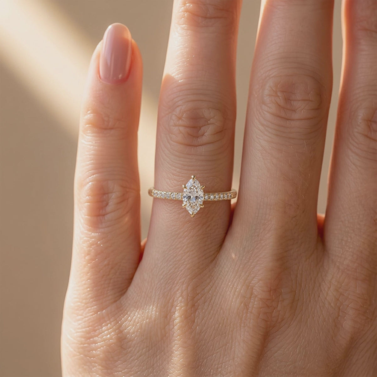 Front view of a hand wearing a gold-tone marquise solitaire ring with a pavé-set band.