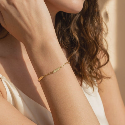 Gold-toned chain bracelet with engraved name plates worn on a woman's wrist.