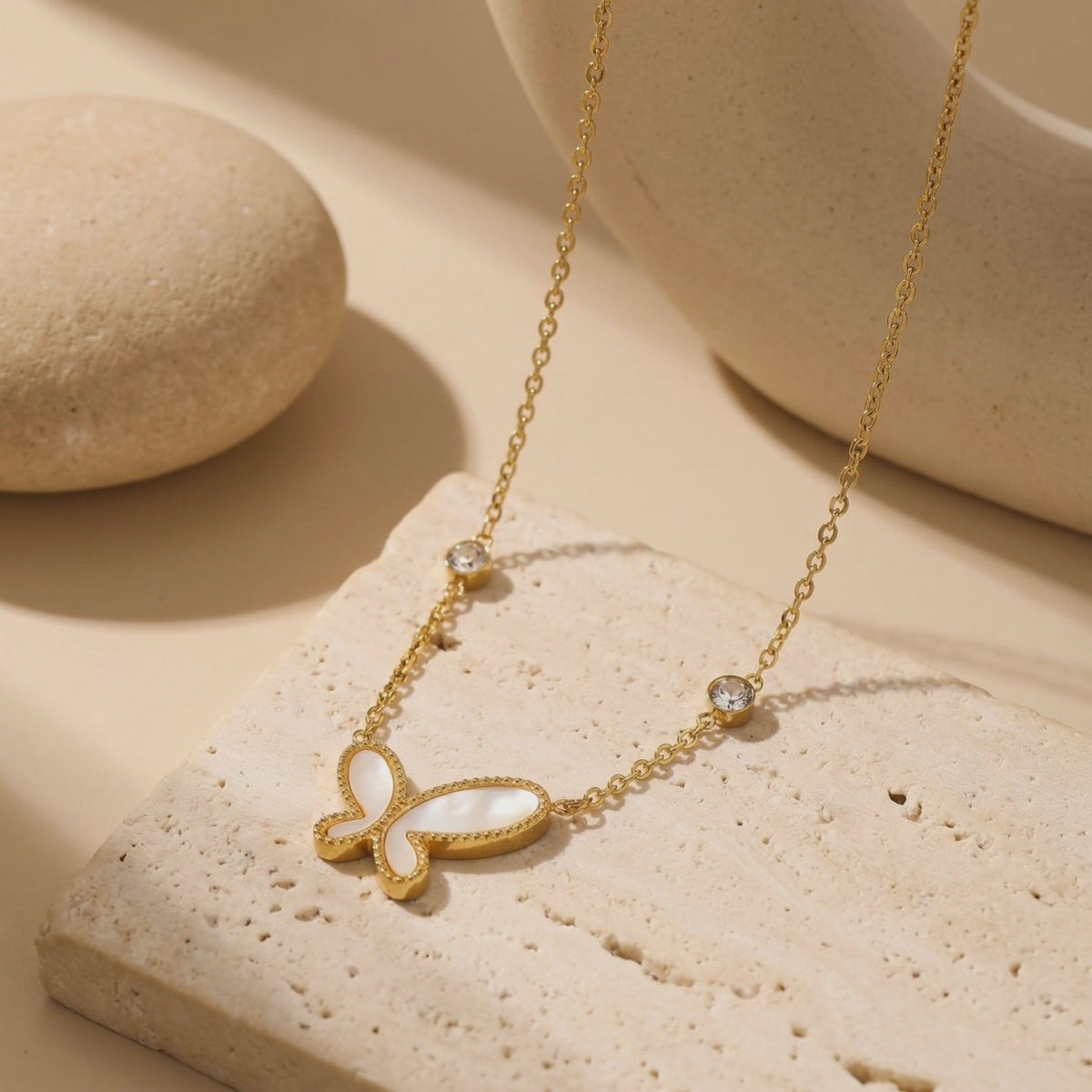 Gold-tone necklace with a mother-of-pearl butterfly pendant, arranged on a textured stone surface