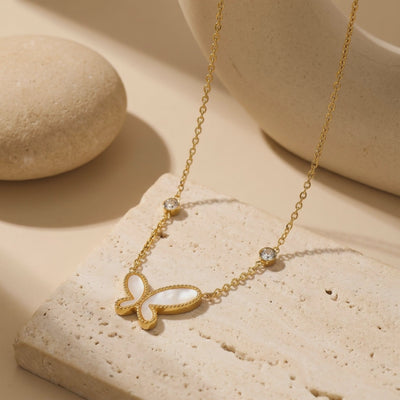 Gold-tone necklace with a mother-of-pearl butterfly pendant, arranged on a textured stone surface