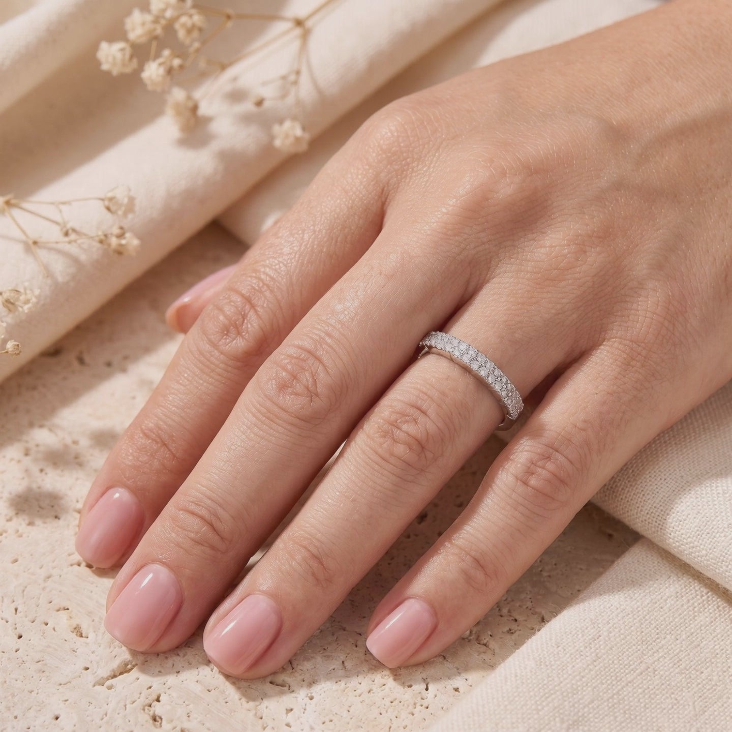 Rosalyssa silver double-row pavé ring worn on a finger against cream fabric and dried flowers.