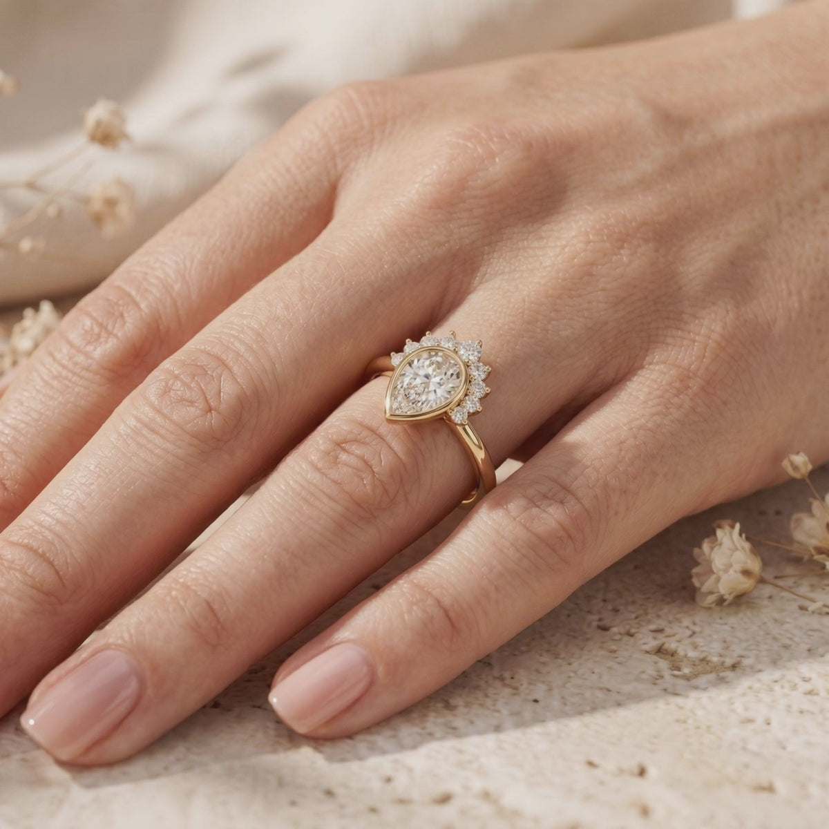 Yellow-gold tone Amaraea ring with a pear-cut moissanite and tiara halo, worn on a hand at an angle.