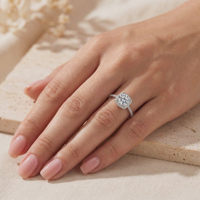 Cushion halo ring worn on a ring finger, showing a round center stone and pavé accent band.