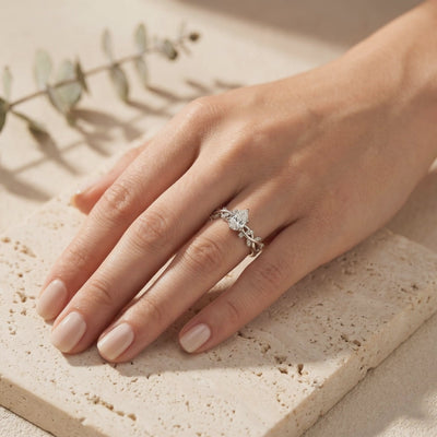 Silver leaf-vine band ring with pear-cut stone worn on a hand over beige stone tile.