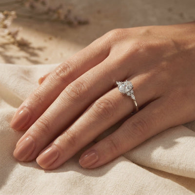 Silver oval moissanite ring with marquise cluster side stones worn on a hand.