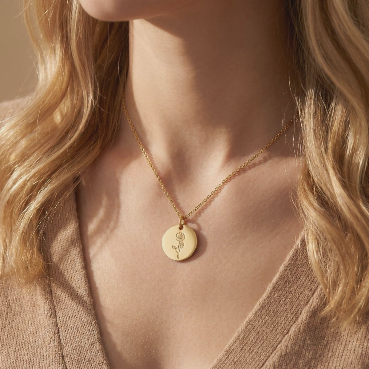 Close-up of a woman wearing a gold-tone necklace with a round engraved birth flower pendant.