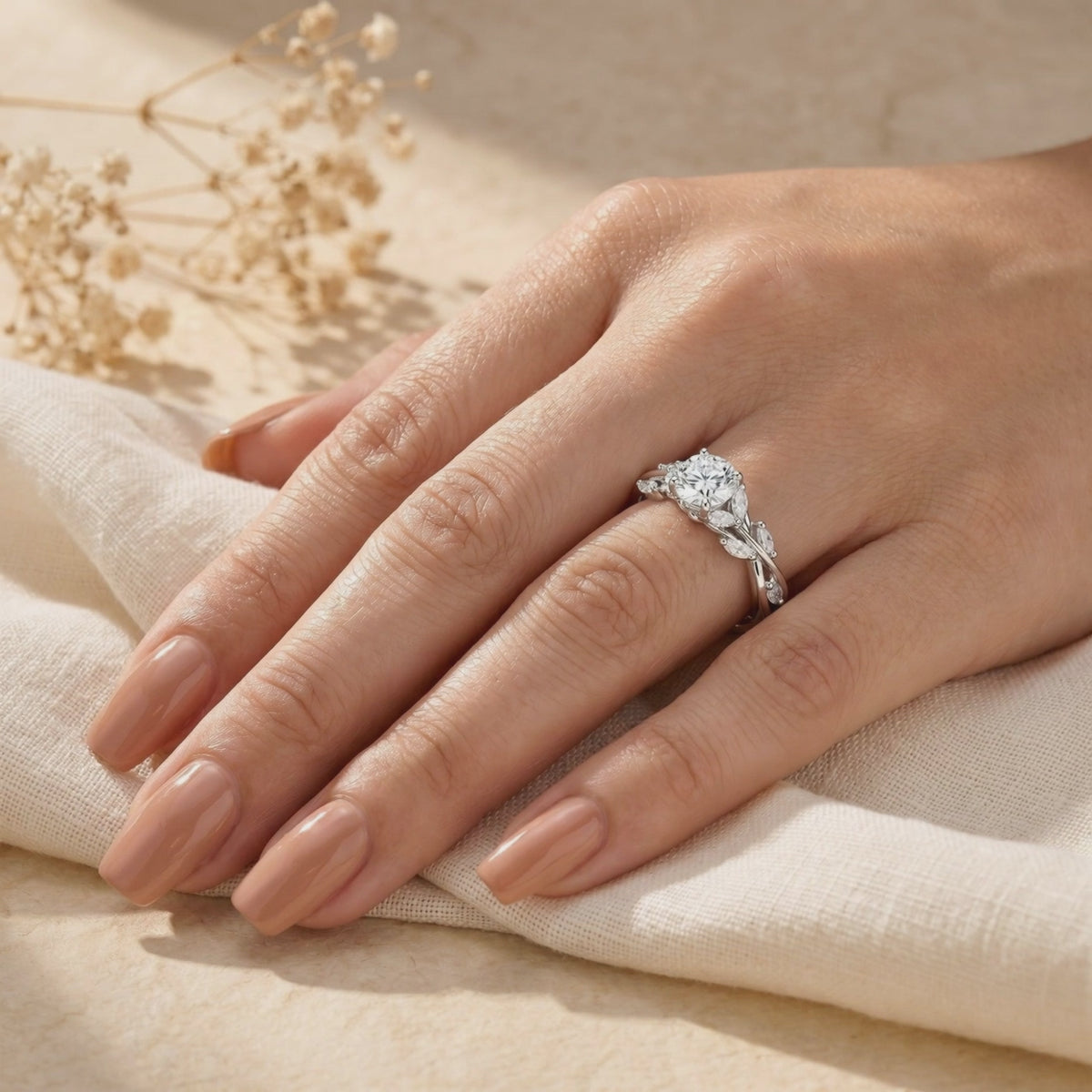 Silver vine moissanite ring worn on a hand resting over beige fabric.
