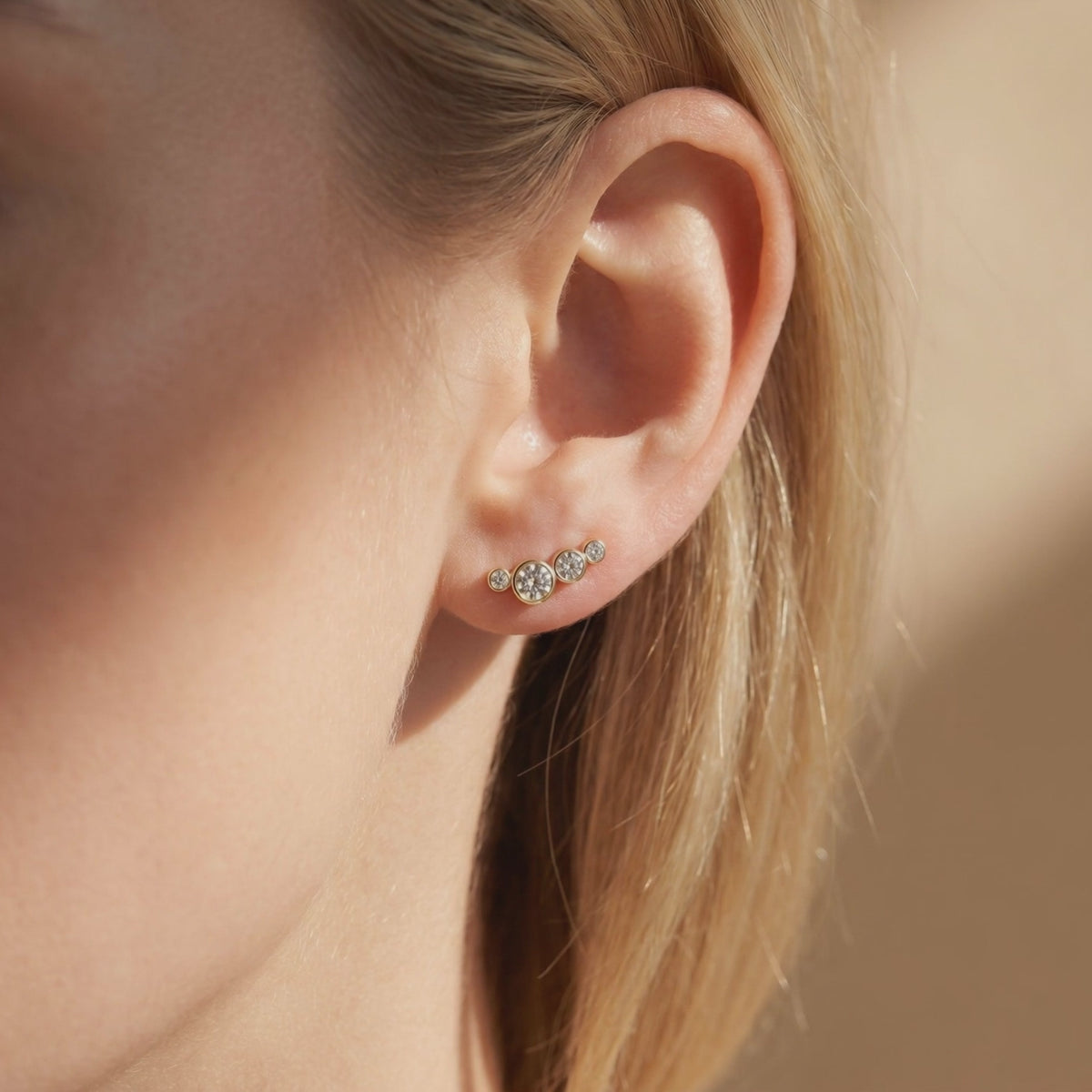 Gold-toned curved moissanite ear climber worn along a woman's earlobe in close-up.