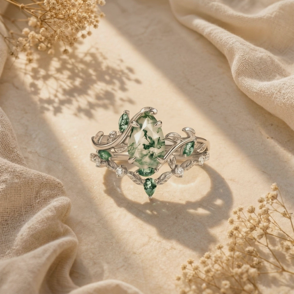Silver vine ring set with pear-cut moss agate and green leaf-like accents arranged upright on a sunlit surface.