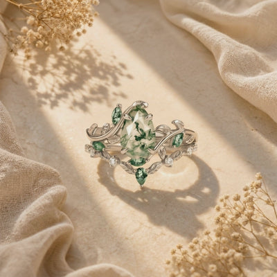 Silver vine ring set with pear-cut moss agate and green leaf-like accents arranged upright on a sunlit surface.
