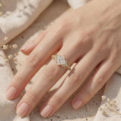 Kite-set princess-cut ring with an accent-studded band worn on a finger over textured fabric.
